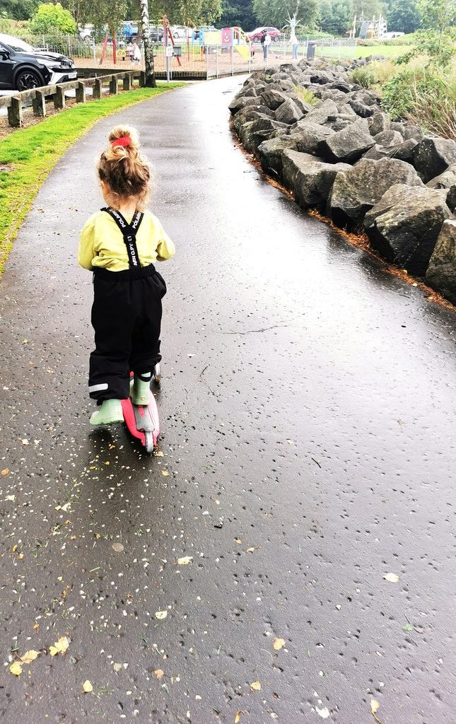 Toddler on Globber scooter on a park path in the rain.